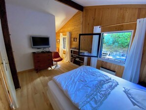 A bedroom with a bed, a television, a chair, and a window with a view of greenery.