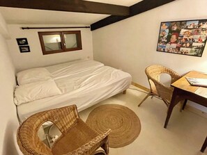 Habitació petita i acollidora amb un llit individual, una taula, dues cadires de vimet i un quadre penjat a la paret.