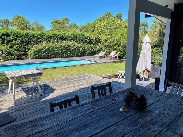 A wooden deck with a pool, lounge chairs, and a covered seating area.