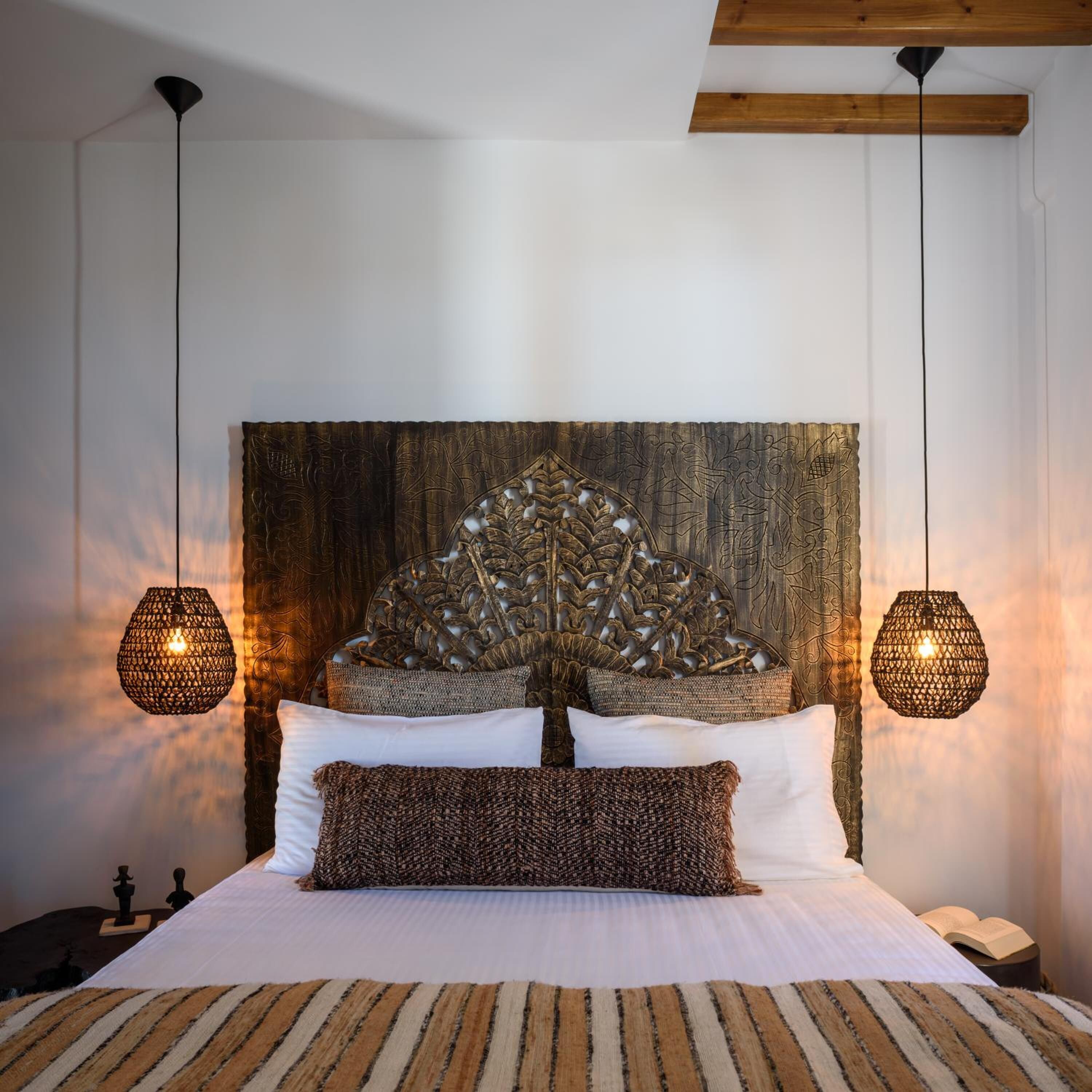 A bed with a decorative headboard, two hanging lamps, and a striped rug.