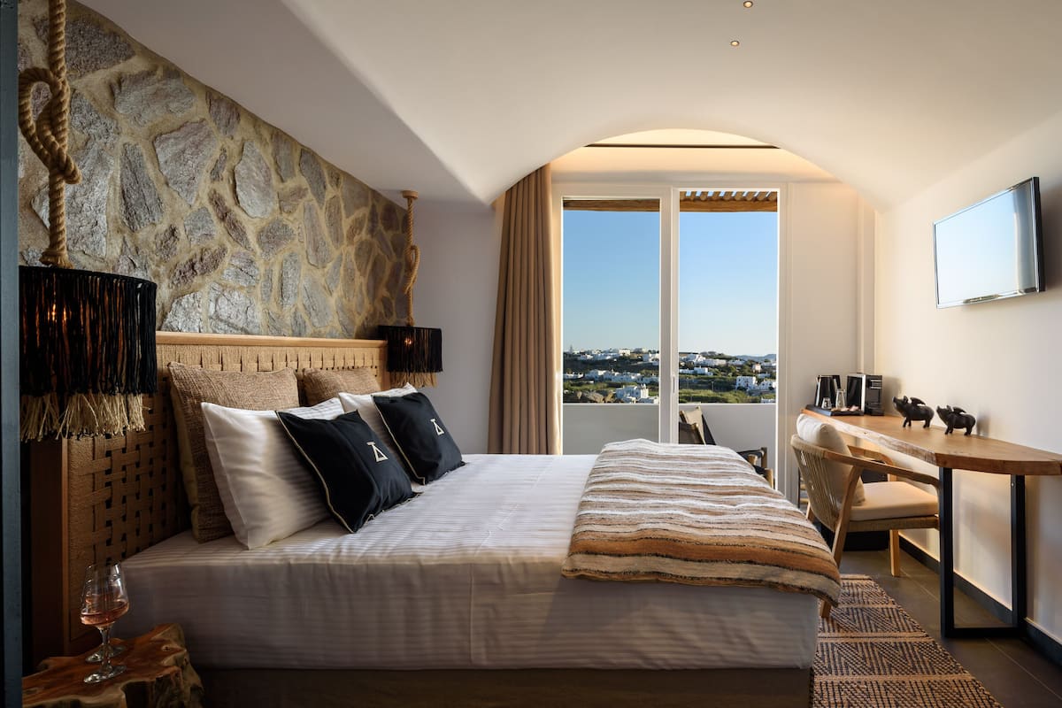 Una habitación de hotel con pared de piedra, una cama con manta a rayas, un escritorio con silla y vistas a la ciudad.