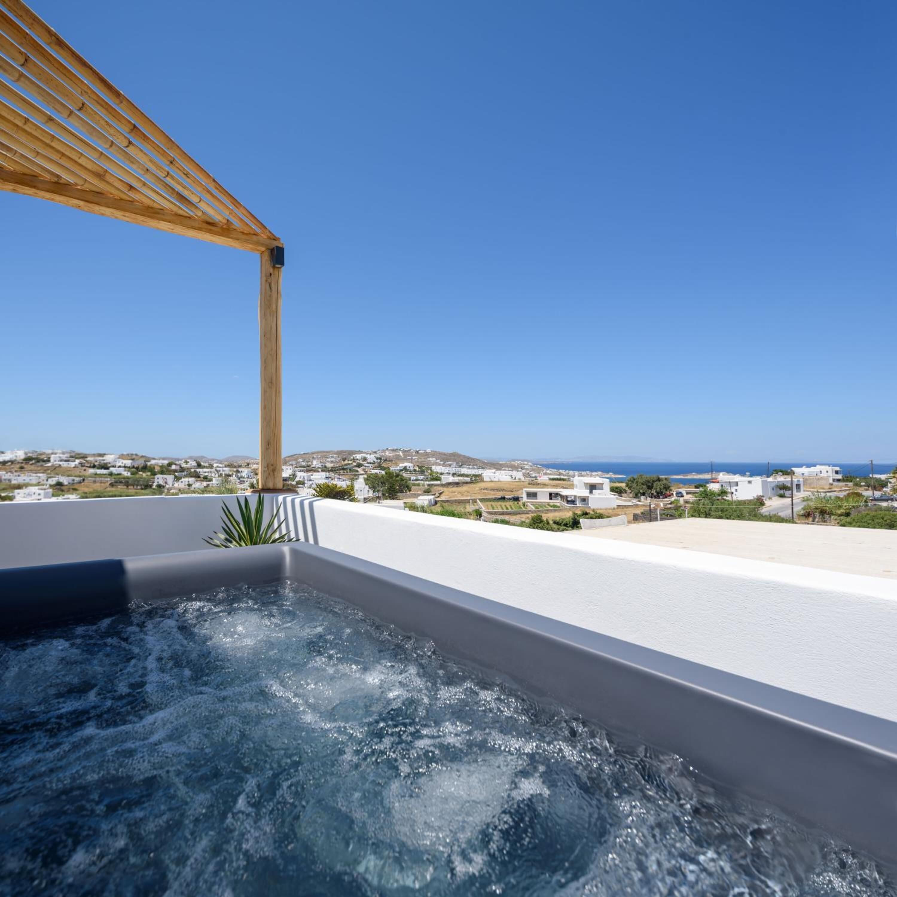 A rooftop terrace with a hot tub, wooden pergola, and a view of a coastal town.