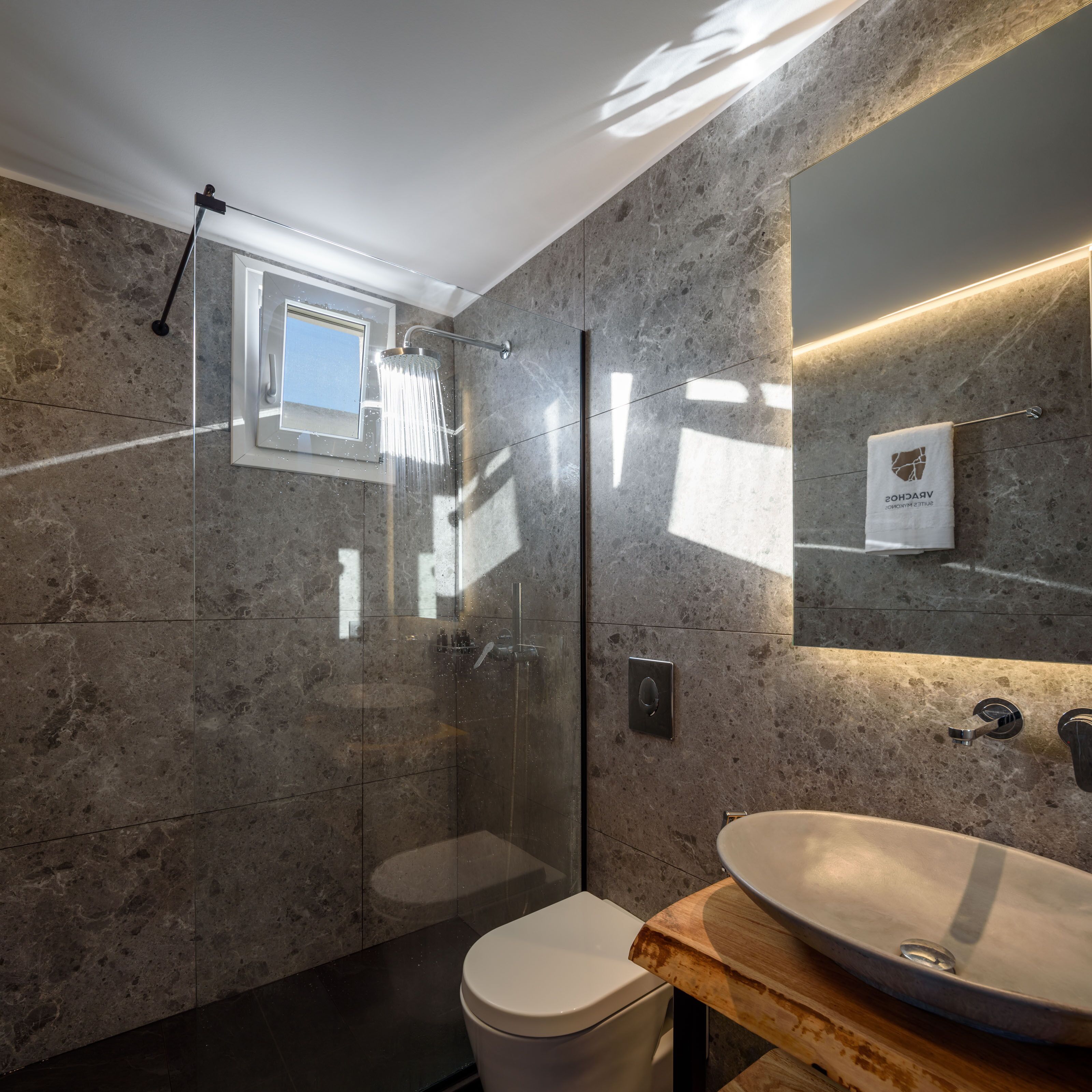 A modern bathroom with a glass-enclosed shower, a white toilet, and a wooden vanity with a large sink.