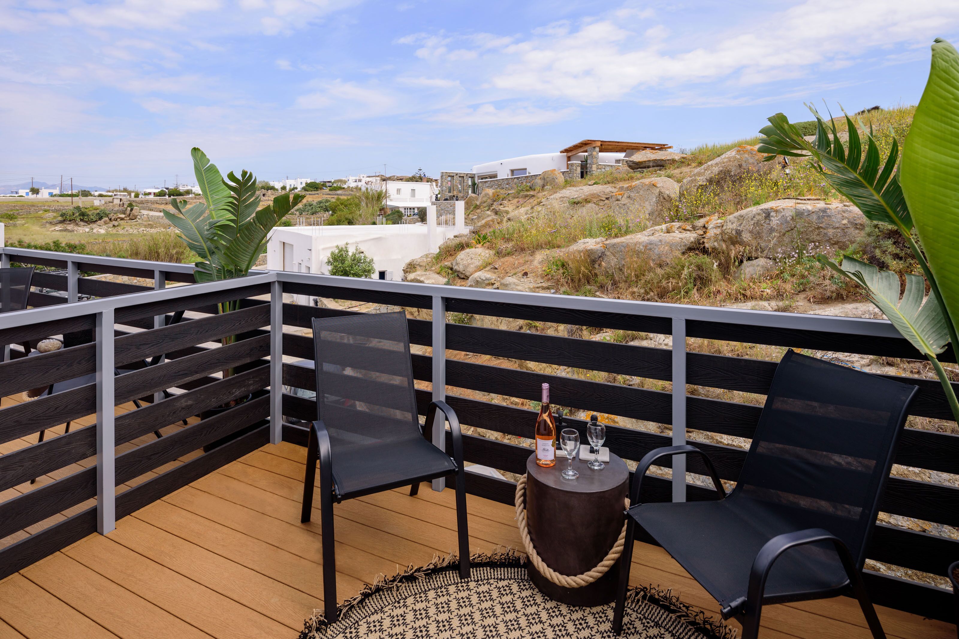 Um terraço com duas cadeiras e uma pequena mesa redonda, uma garrafa de vinho e copos na mesa.