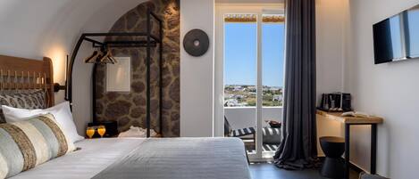 A bedroom with a bed, a desk, a chair, and a view of the outside.