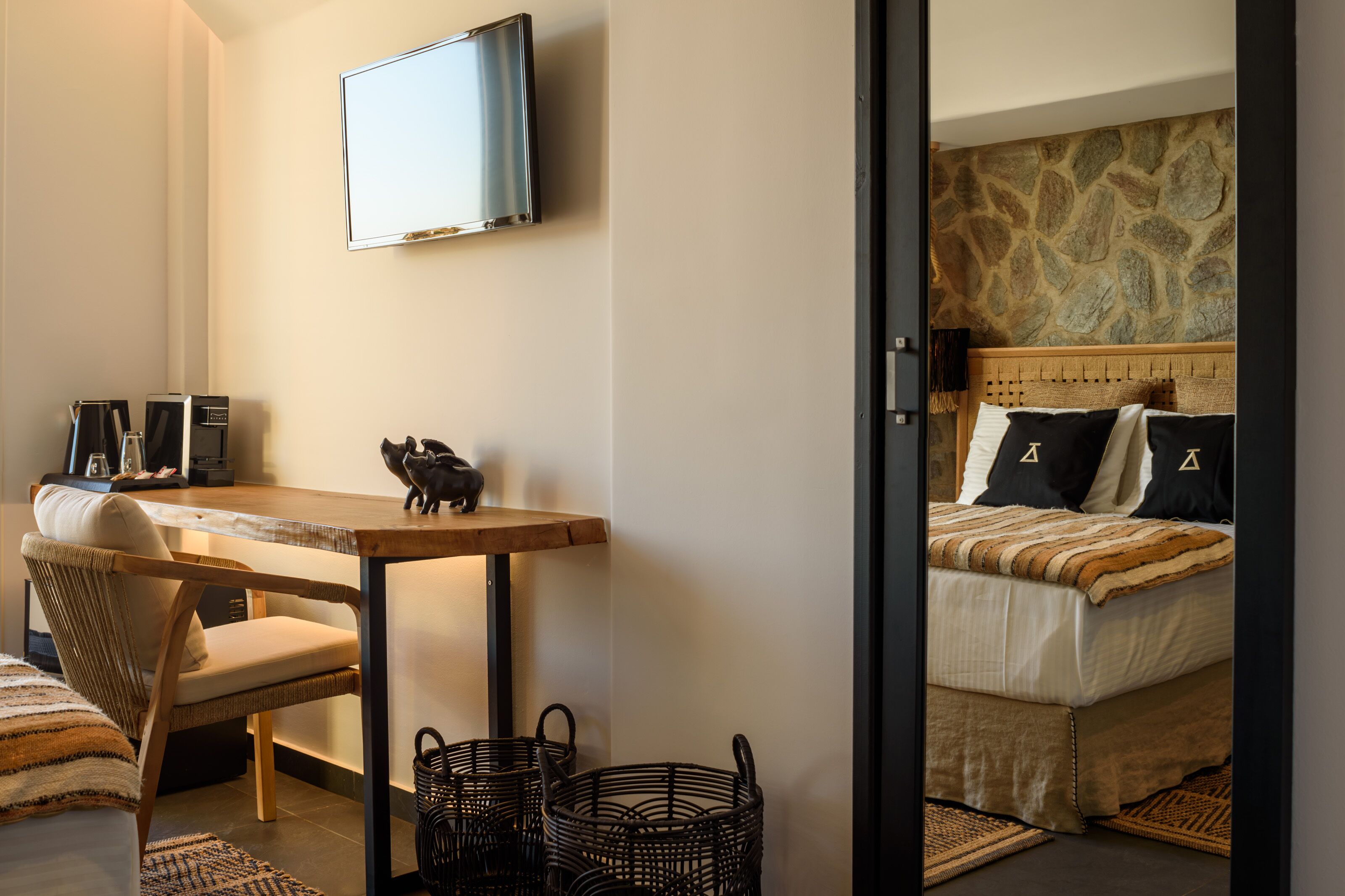 Een slaapkamer met een bed, een aan de muur bevestigde televisie, een houten tafel, een stoel en rieten manden.