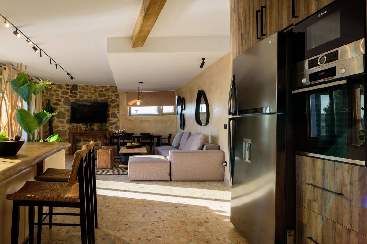 Una cocina con pared de piedra, barra de madera y un refrigerador grande.