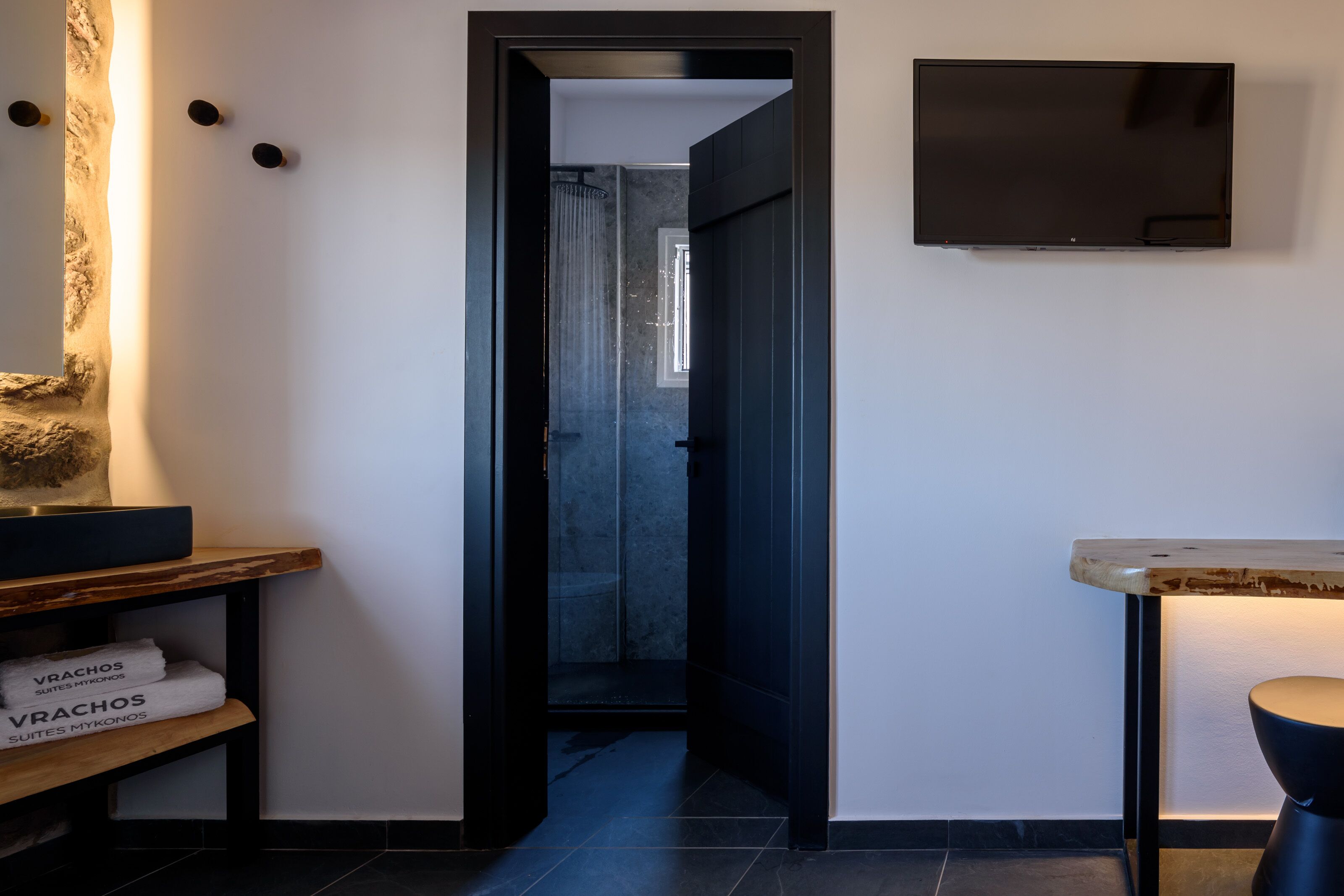 Un baño moderno con ducha, un televisor de pantalla plana montado en la pared y un estante de madera con toallas.