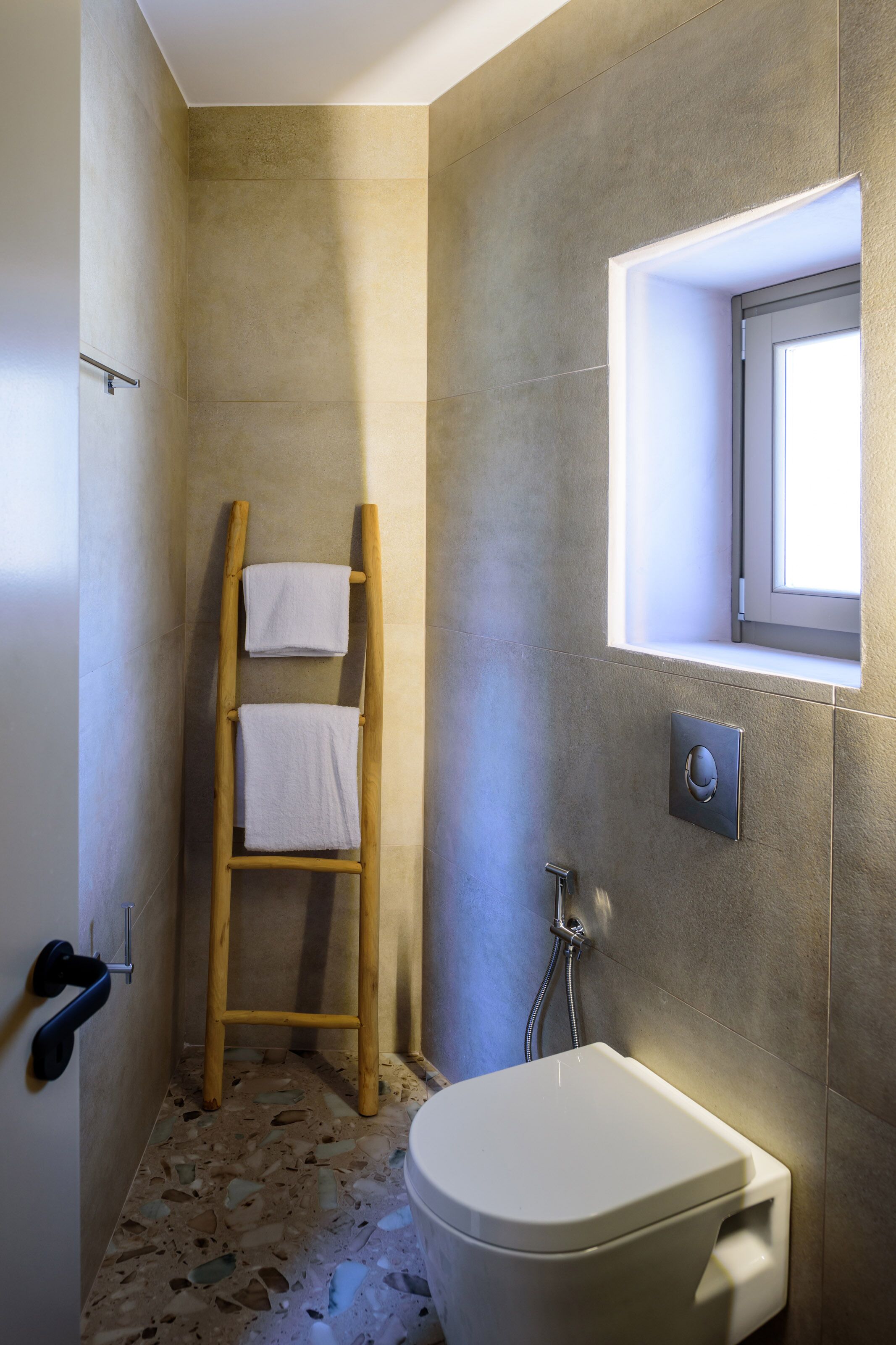 A bathroom with a shower, a toilet, a wooden ladder, and a window.