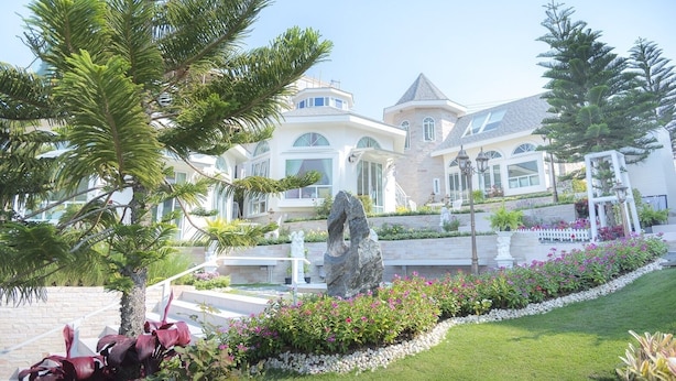 Una casa grande y moderna con un jardín bien cuidado, que incluye una fuente y diversas plantas.
