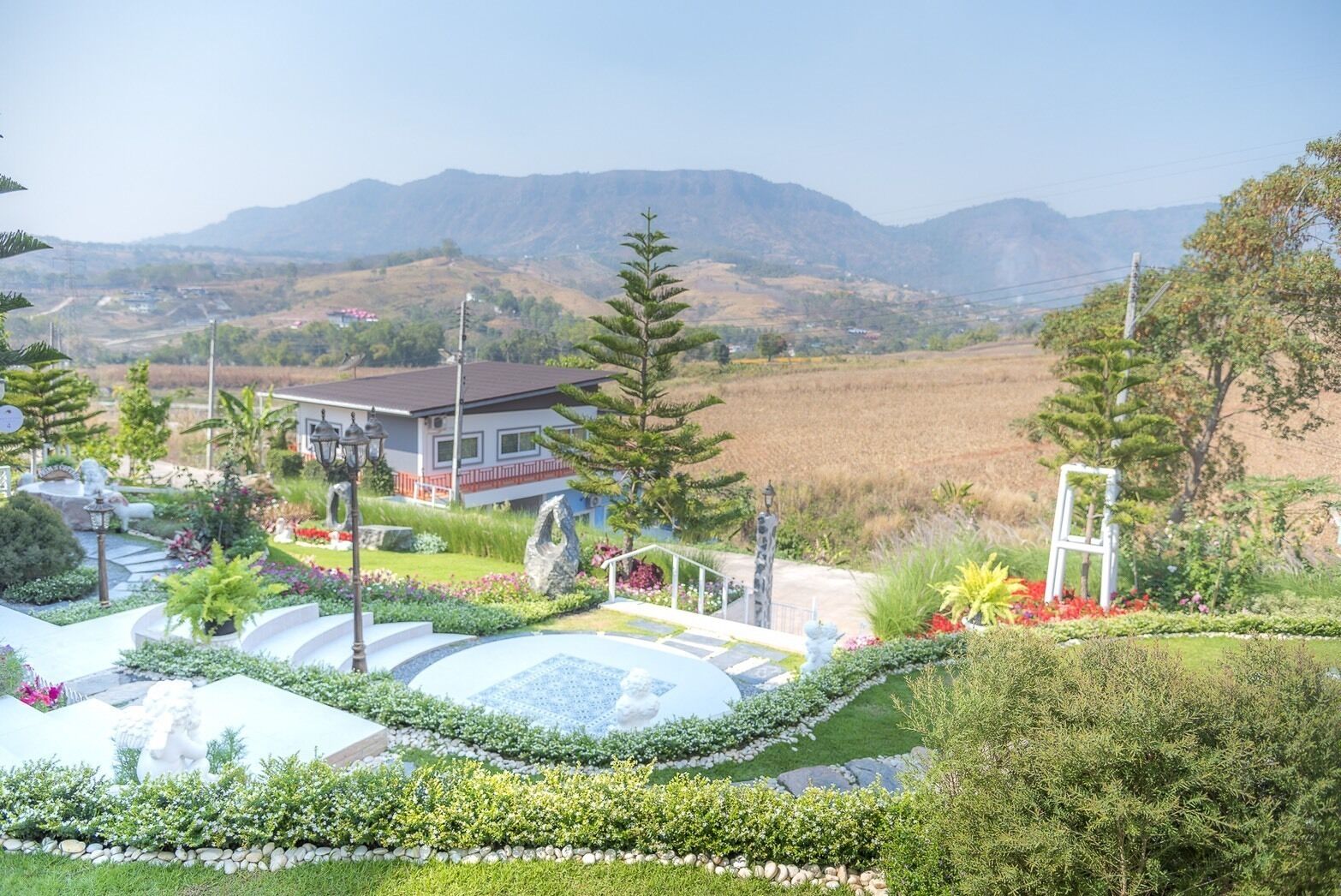 A landscaped garden with a fountain, a house, and mountains in the background.