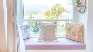 Asiento junto a la ventana con cojines y un cojín de macramé, con vistas a un paisaje pintoresco.
