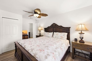 A bedroom with a wooden bed, a ceiling fan, two bedside lamps, and a white door.