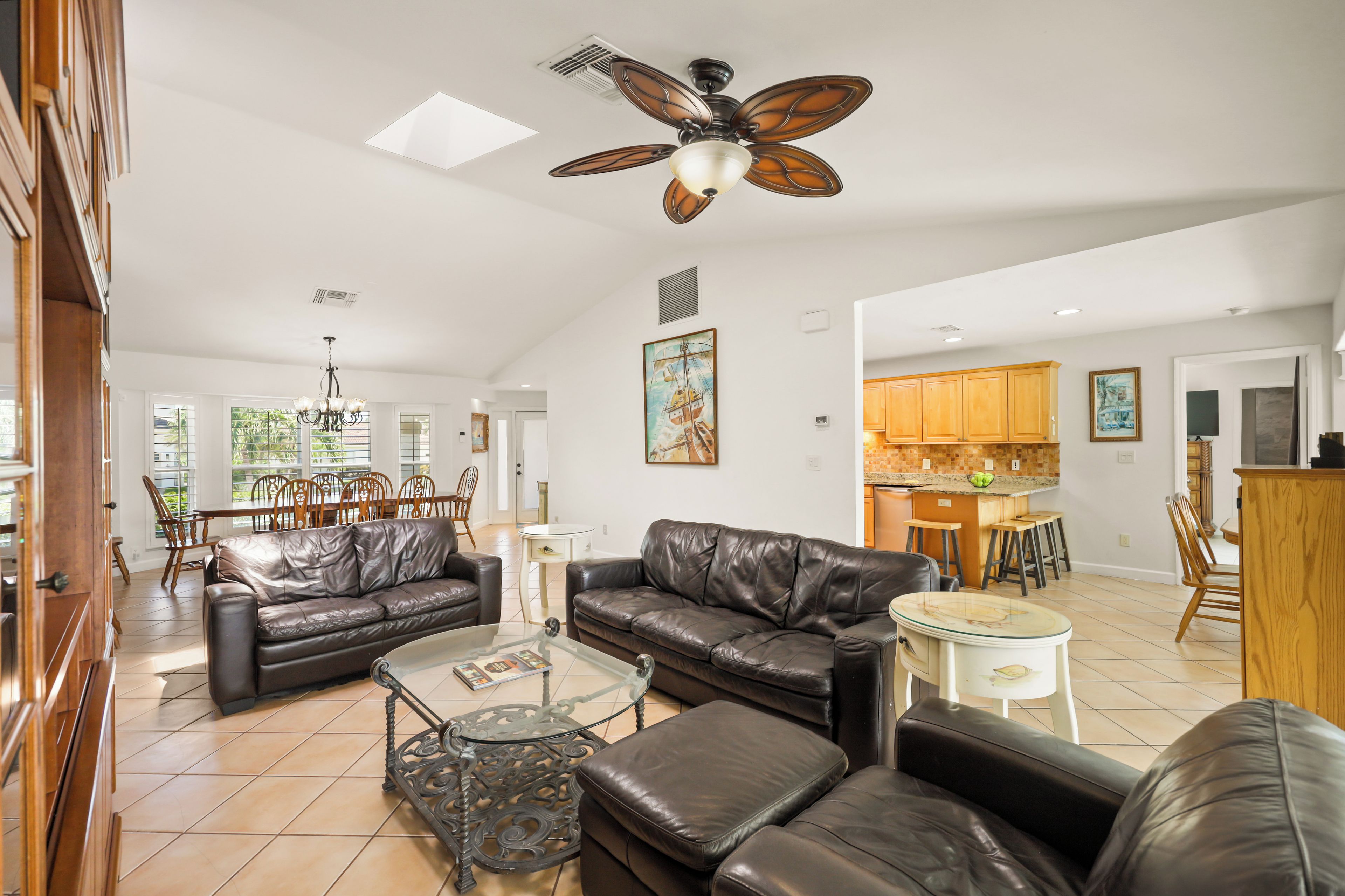 A spacious living area with leather sofas, a glass coffee table, and a ceiling fan.
