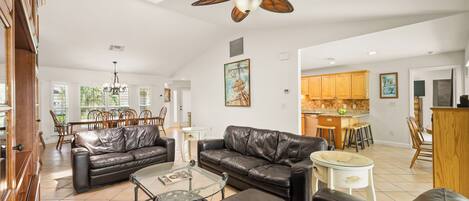 A spacious living area with leather sofas, a glass coffee table, and a ceiling fan.