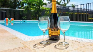 Uma garrafa de champanhe Ariel Brut Cuvée e duas taças sobre uma mesa à beira da piscina, com uma piscina ao fundo.