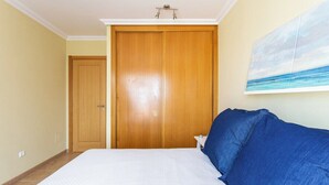 A bedroom with a large bed, a wooden wardrobe, and a painting of a beach scene. - Home2Book La Tejita Beach and Pool (Granadilla)
