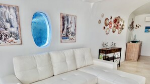 Un salon moderne avec un canapé d’angle blanc, un buffet en bois et des œuvres d’art murales, notamment un ovale bleu et des tableaux sur le thème de la marine.
