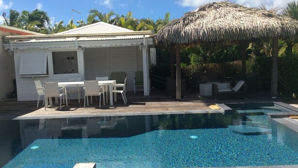 A swimming pool with a wooden deck, a covered seating area, and a thatched roof structure.