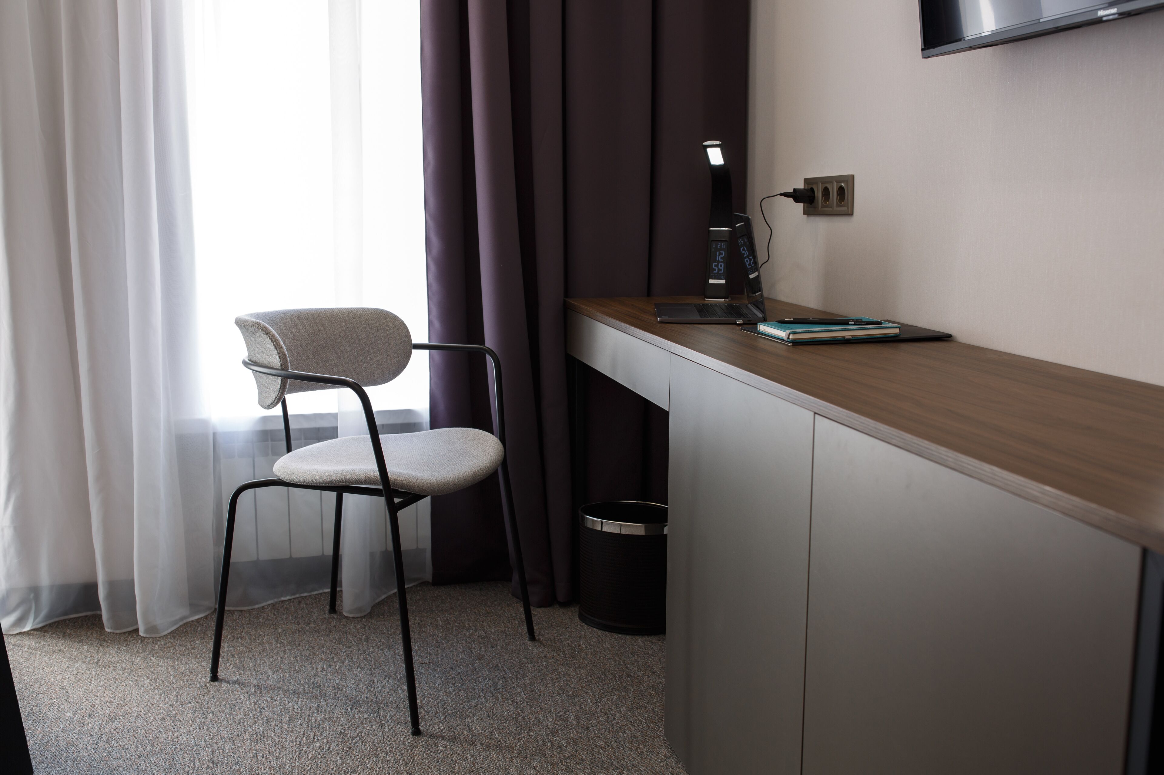 A hotel room with a desk, chair, and a TV mounted on the wall.
