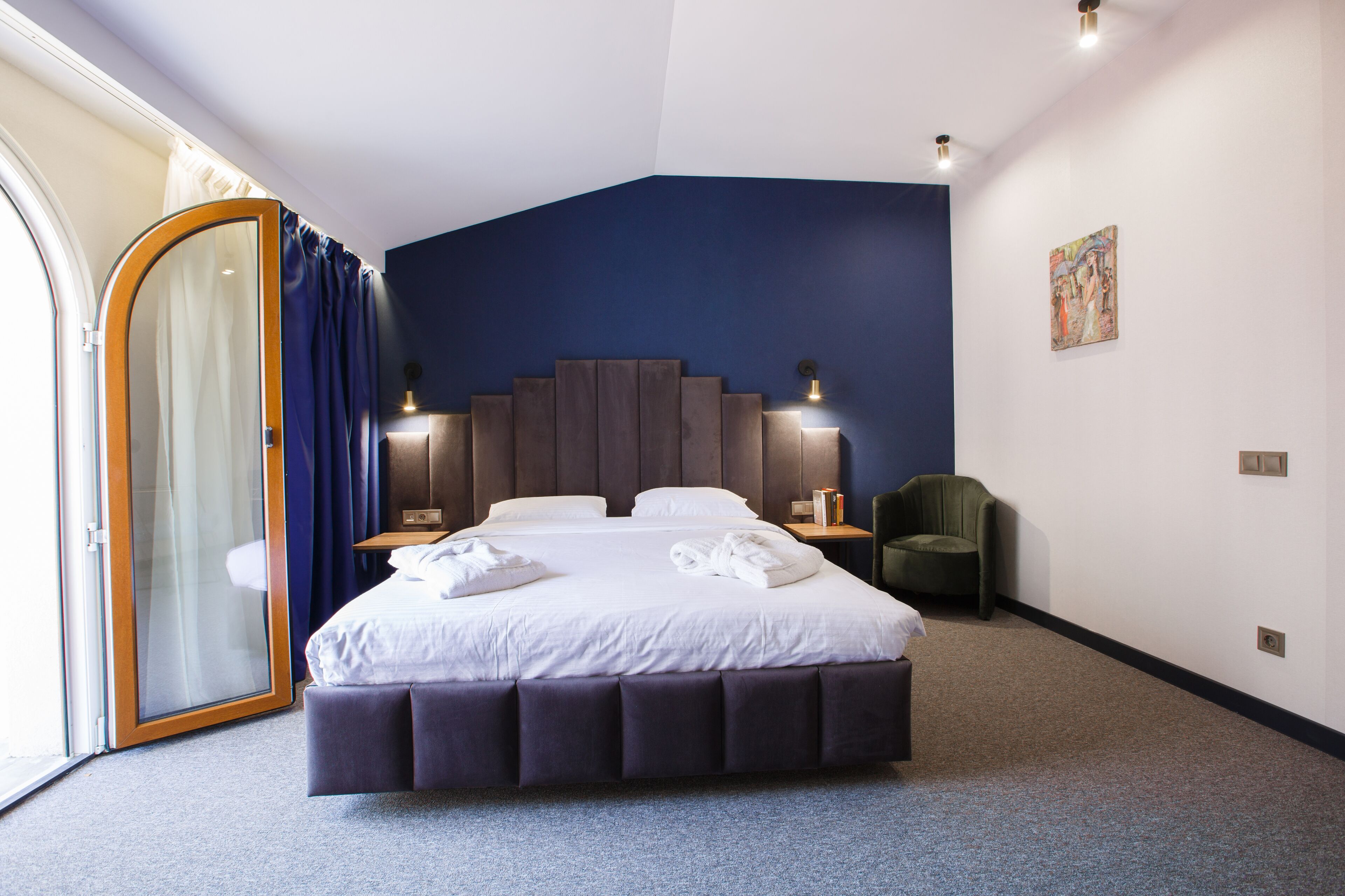 Una habitación de hotel moderna con una cama grande, una puerta corrediza de vidrio, una pared de acento azul oscuro y una pequeña zona de estar.