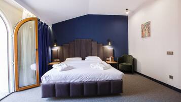 Una habitación de hotel moderna con una cama grande, una puerta corrediza de vidrio, una pared de acento azul oscuro y una pequeña zona de estar.