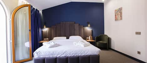 A modern hotel room with a large bed, a sliding glass door, a dark blue accent wall, and a small seating area.