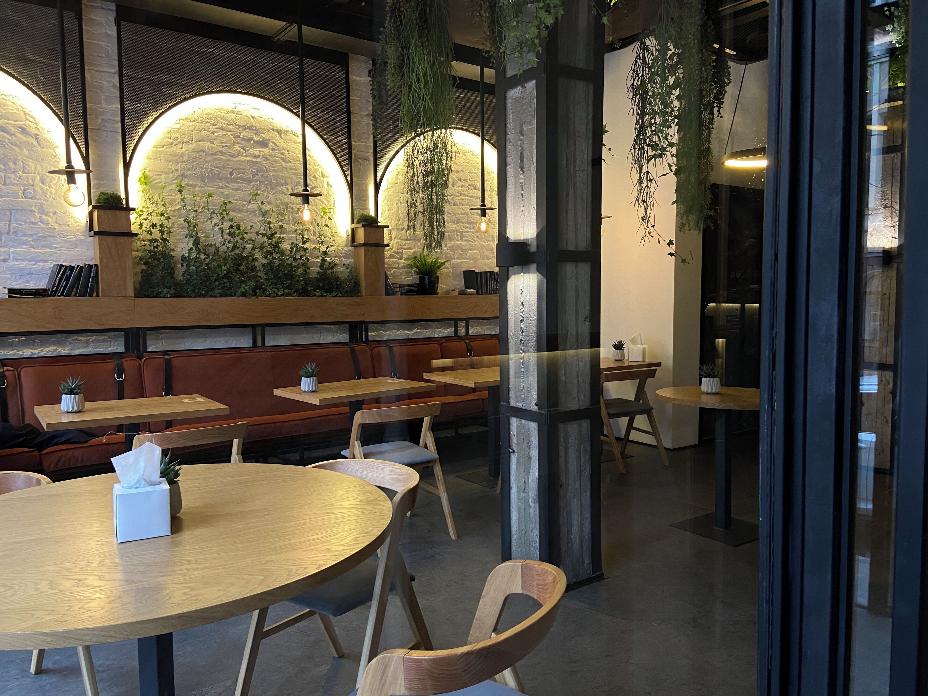 A restaurant interior with round tables, wooden benches, and hanging plants.