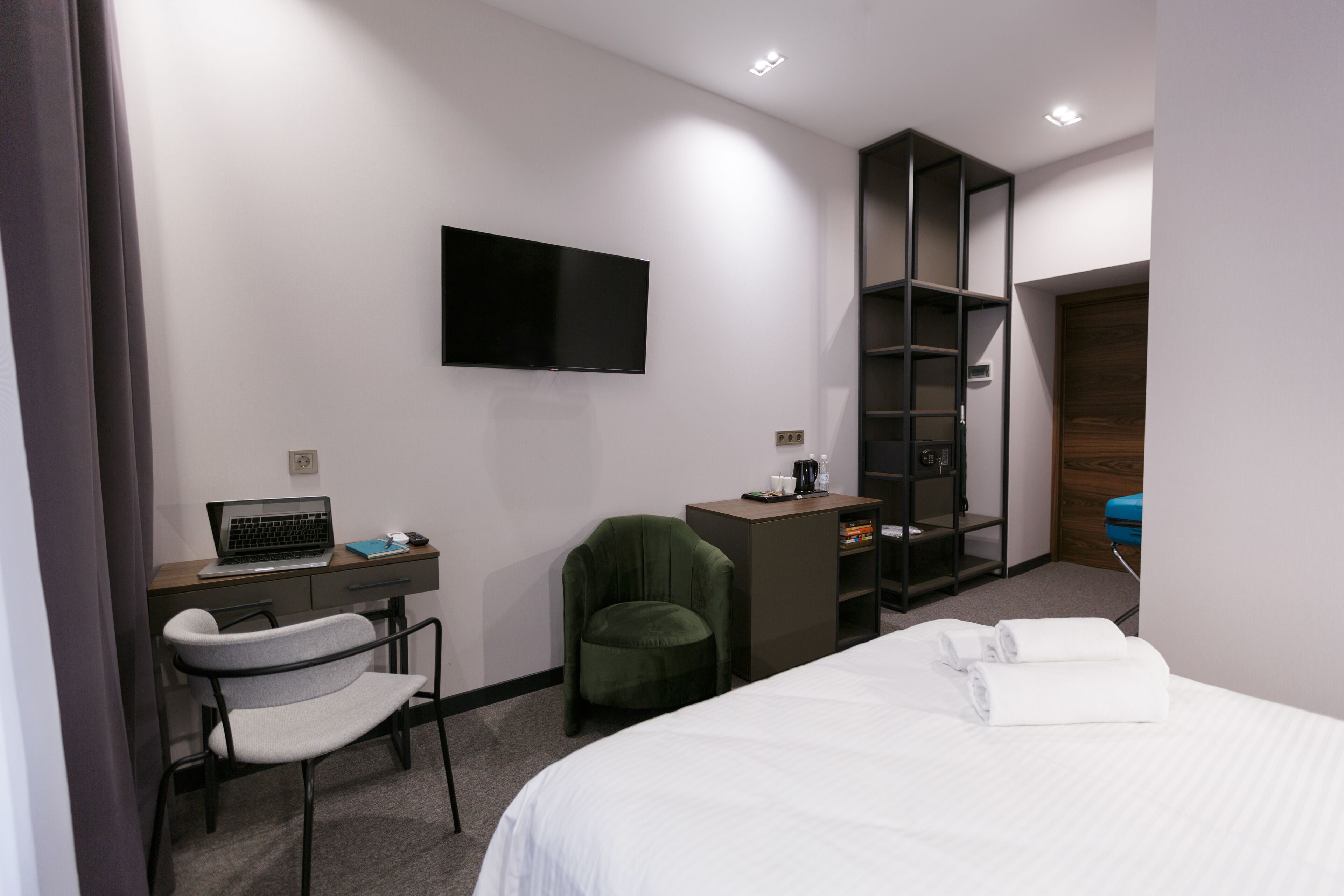 Habitación de hotel con cama, escritorio con computadora portátil, silla, televisor en la pared y armario.