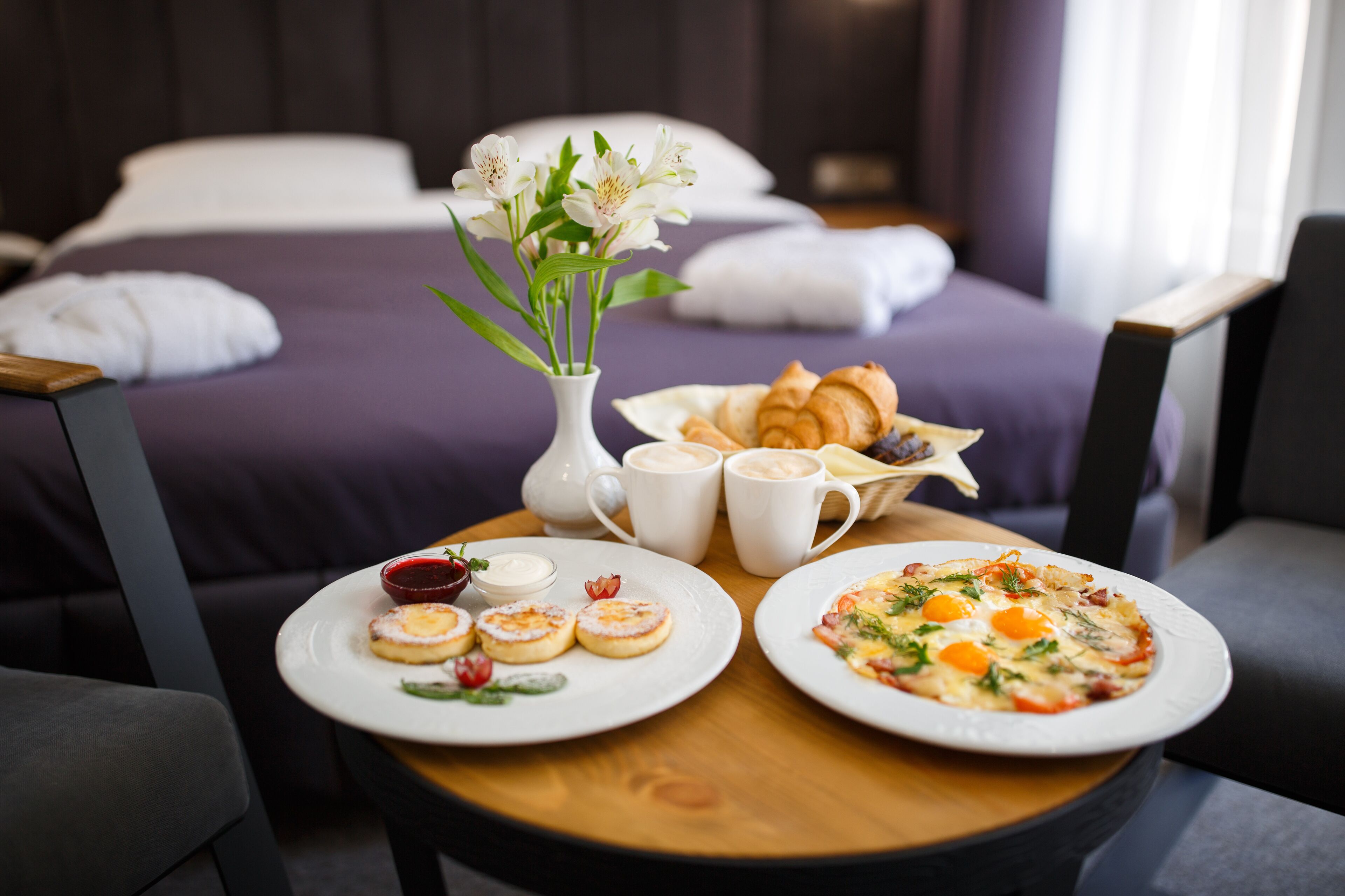 A breakfast setup with croissants, pastries, and a pizza on a wooden table in a hotel room.