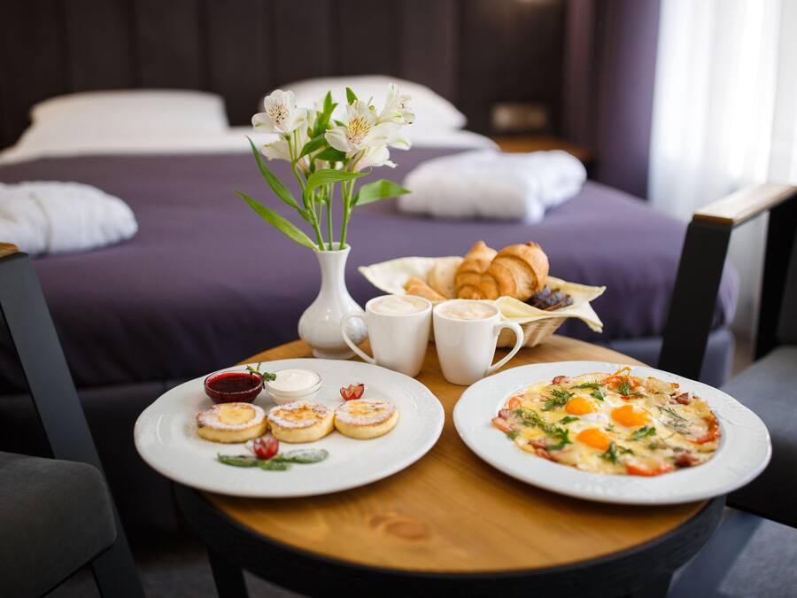 A breakfast setup with croissants, pastries, and a pizza on a wooden table in a hotel room.