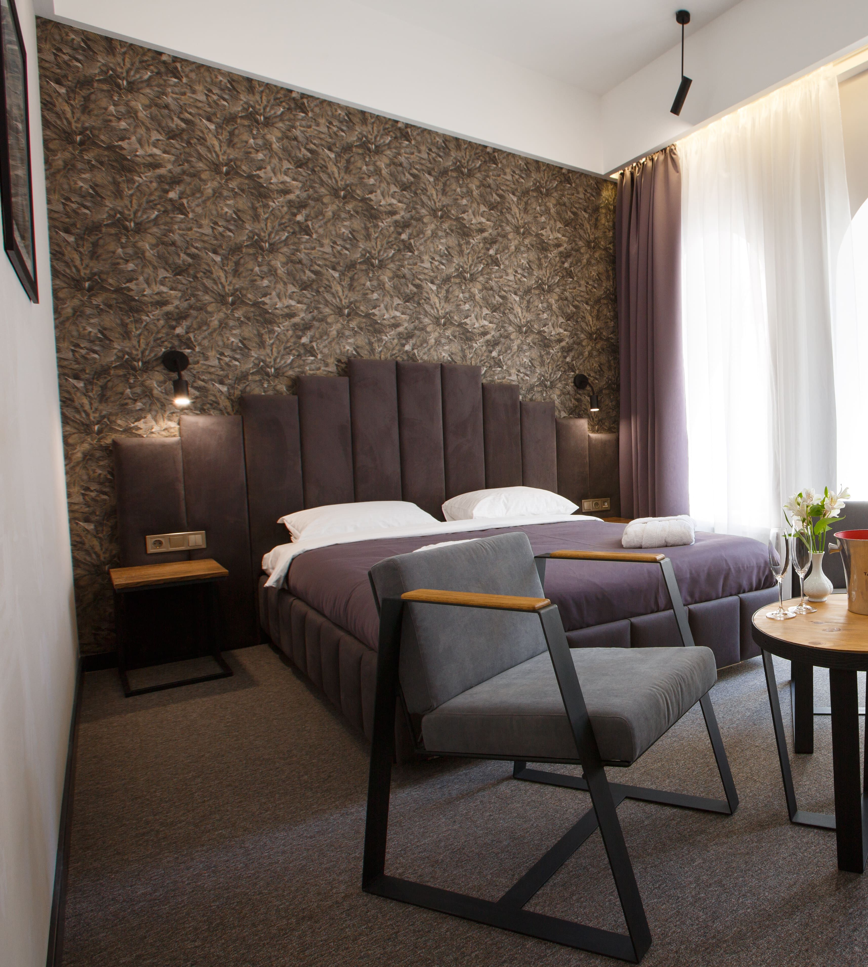 A modern bedroom with a large bed, a nightstand, a chair, a small table, and a decorative vase.