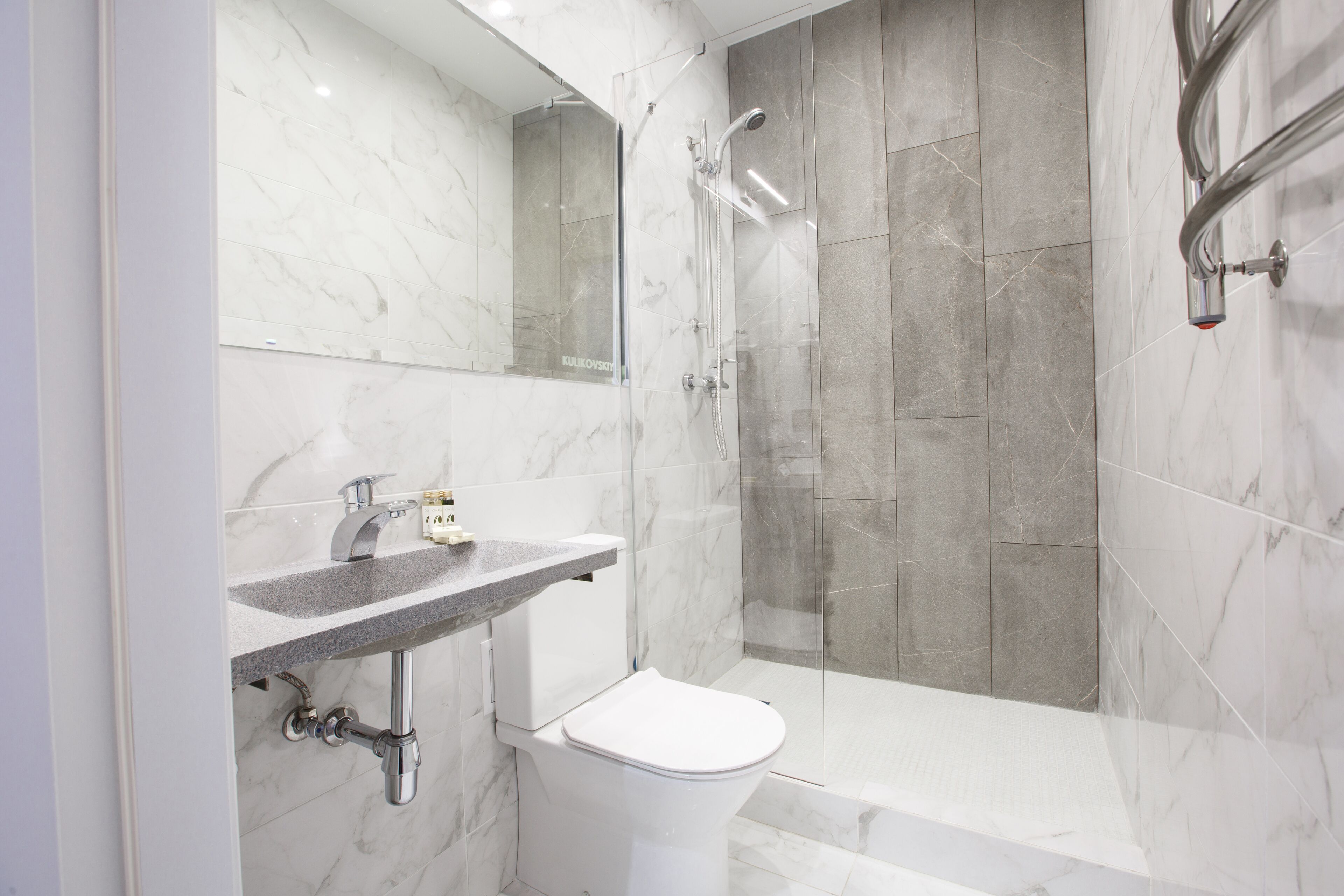 A modern bathroom with a marble sink, a toilet, and a glass-enclosed shower area.