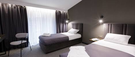 Habitación de hotel con dos camas, una silla, un escritorio y una ventana con cortinas.