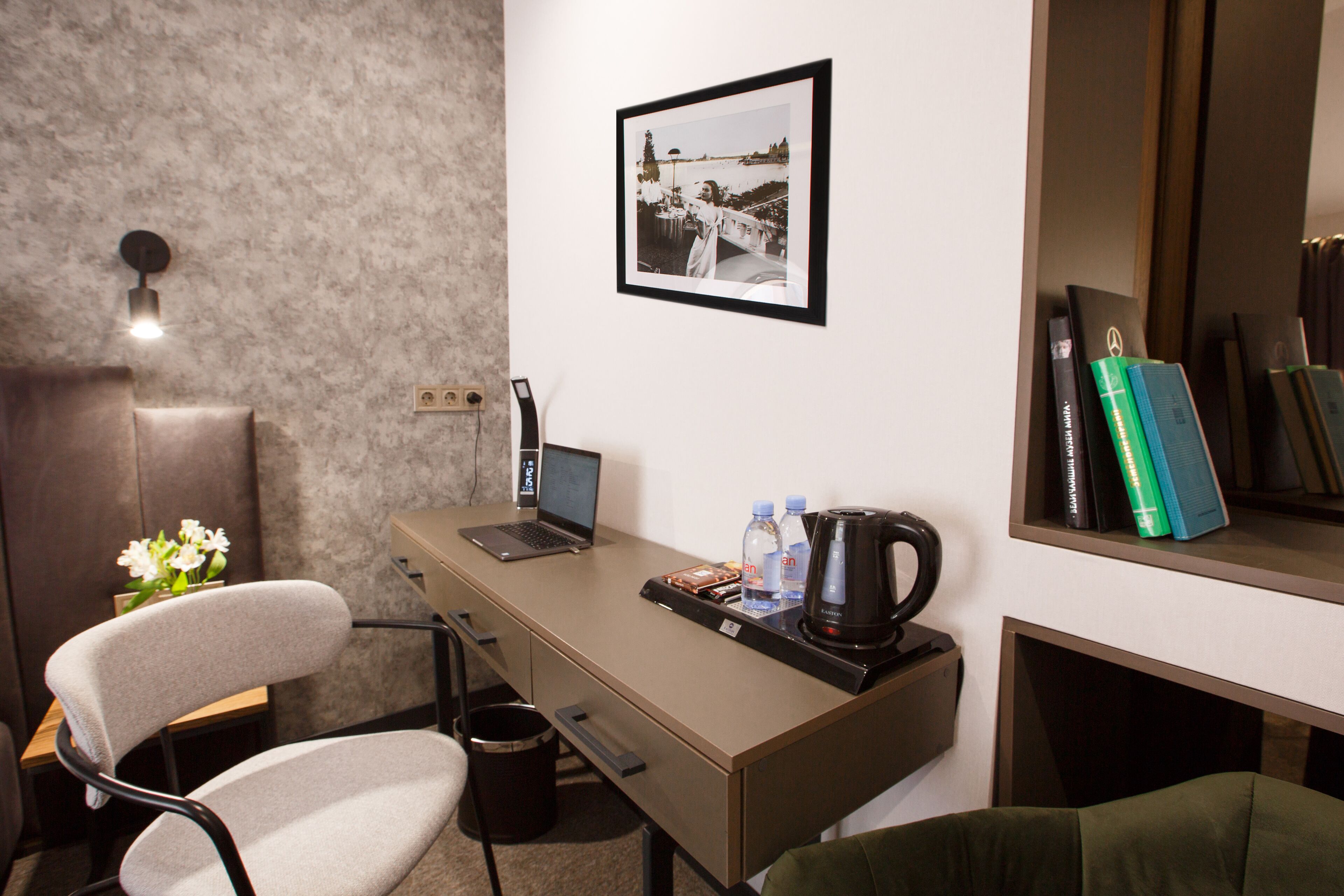 A modern hotel room with a desk, laptop, coffee maker, and a framed photo on the wall.