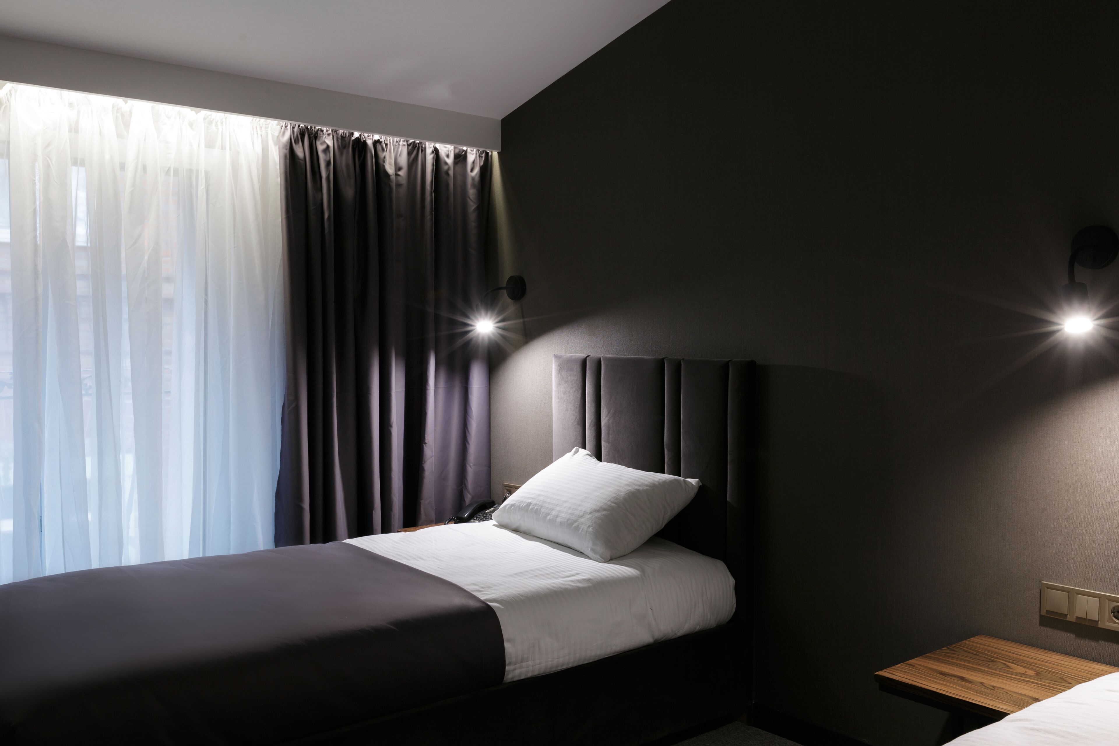 Une chambre d’hôtel moderne équipée d’un lit, d’une table de chevet, d’une commode et d’une fenêtre avec des rideaux.
