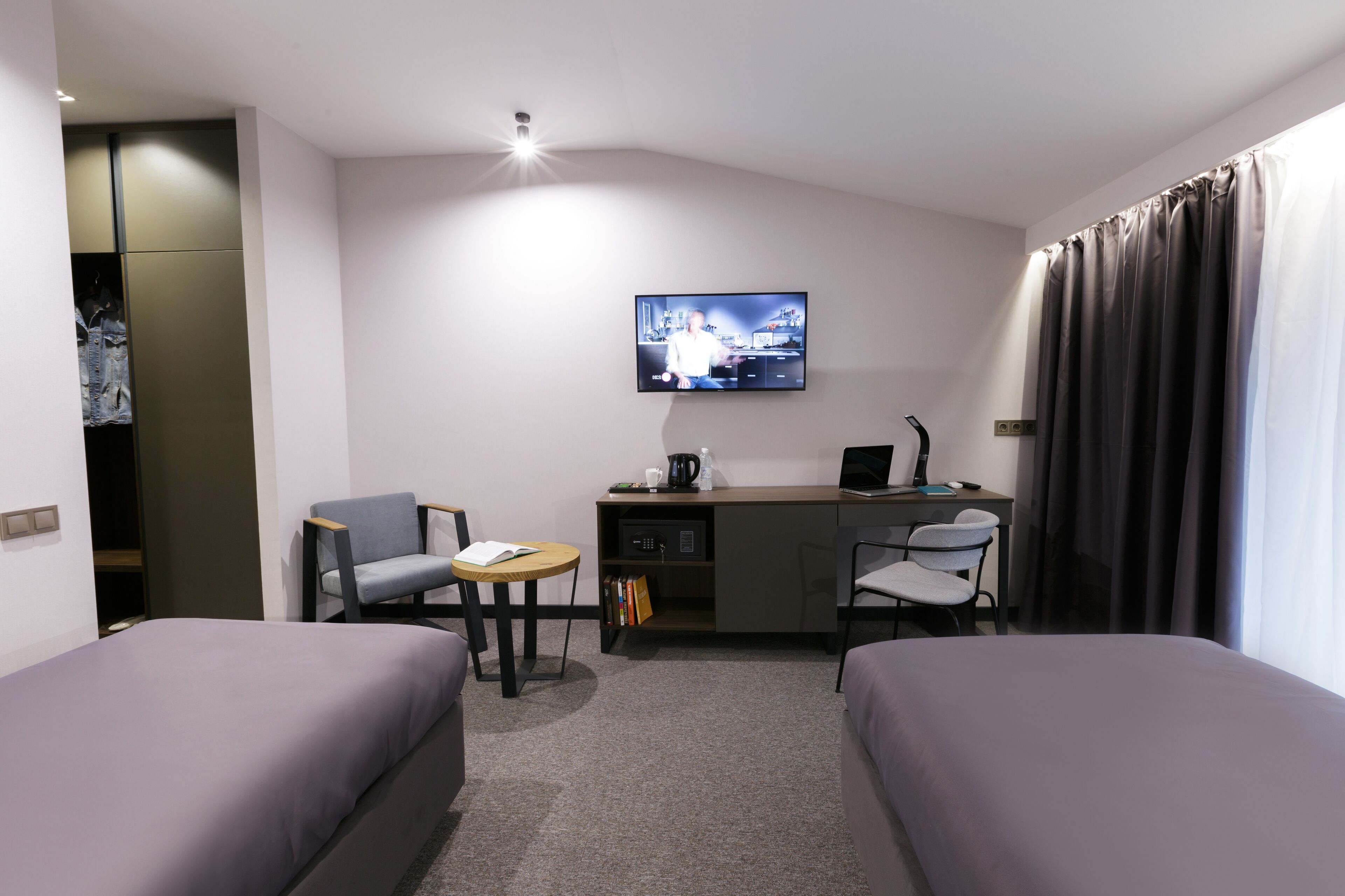 A hotel room with two beds, a desk with a computer, a chair, a TV, and a small table.
