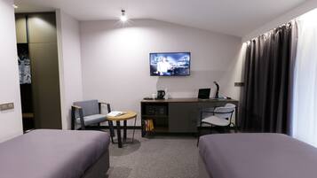 A hotel room with two beds, a desk with a computer, a chair, a TV, and a small table.