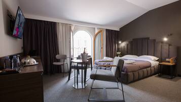 A hotel room with a bed, a desk, a chair, a small table, and a TV.
