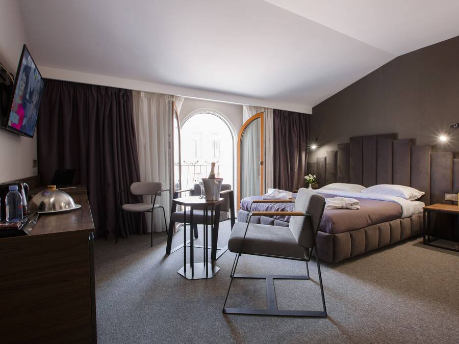 A hotel room with a bed, a desk, a chair, a small table, and a TV.