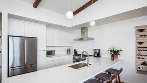 Una cocina moderna con armarios blancos, un refrigerador de acero inoxidable, una estufa a gas y una barra con taburetes.