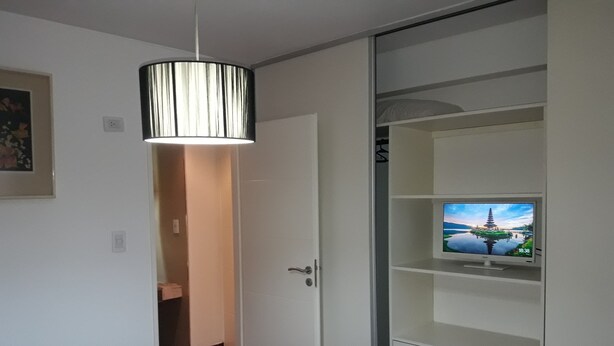 Ein Schlafzimmer mit einem Bett, einem Fernseher auf einem Regal und einer Tür zu einem Badezimmer.
