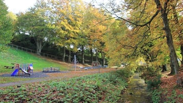 A park with playground equipment, a grassy slope, and a stream.