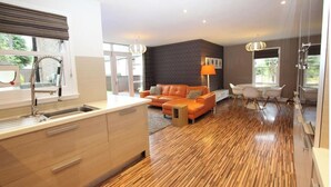 Une cuisine moderne dotée d’un îlot central intégré, un coin repas avec une table et des chaises, et un salon avec un canapé et une lampe.