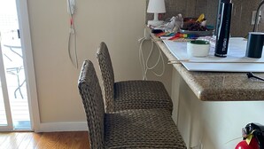 A kitchen with a wicker chair, a white air conditioning unit, a fire extinguisher, and a countertop with various items.