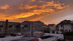 A residential area with multiple two-story houses, a parking lot with several cars, and a clear view of the sky with clouds.