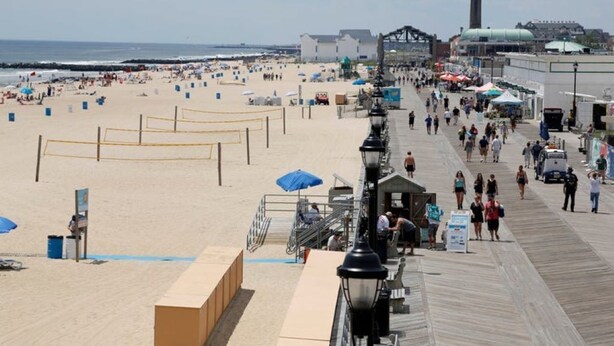 A beach with a boardwalk, umbrellas, and people walking.