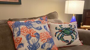 A brown sofa with two decorative pillows, one with a blue and orange crab pattern and the other with a multicolored abstract design.