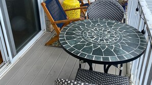 A balcony with a round table, two chairs, and a yellow stool.