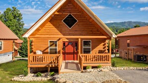 Une cabane en bois avec une porte rouge, un balcon et un petit porche.